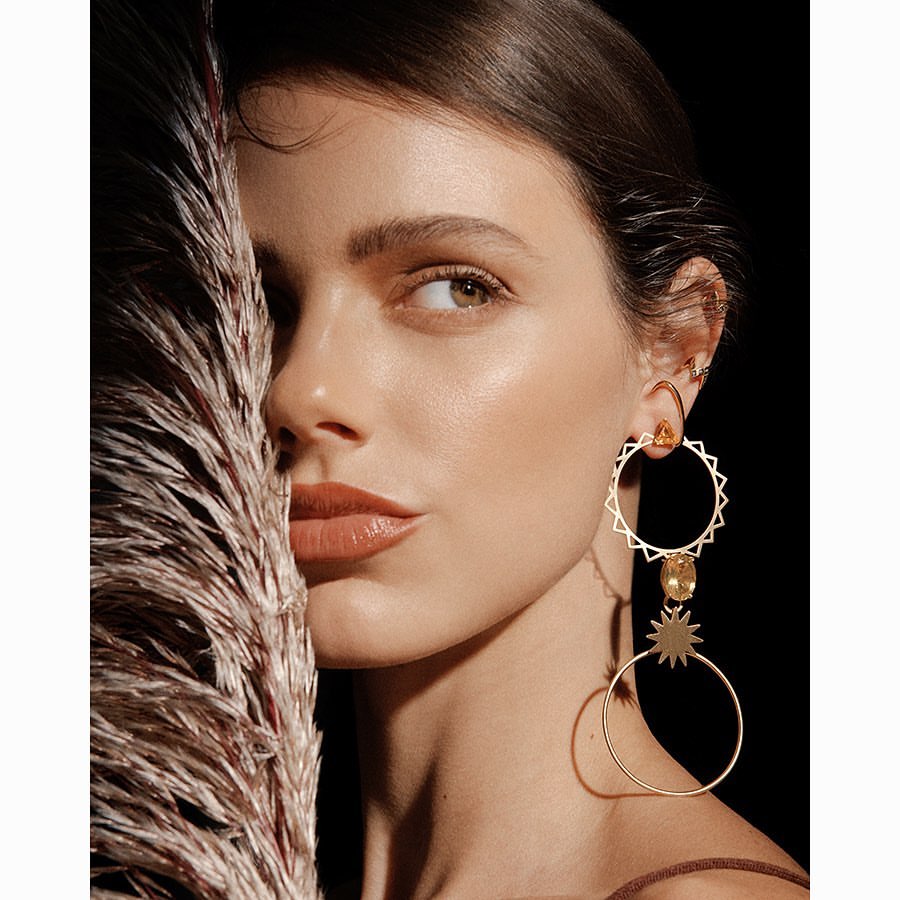 Close-up of a woman with fair skin and brown hair, looking to the left, posing with decorative pampas grass and wearing long earrings.