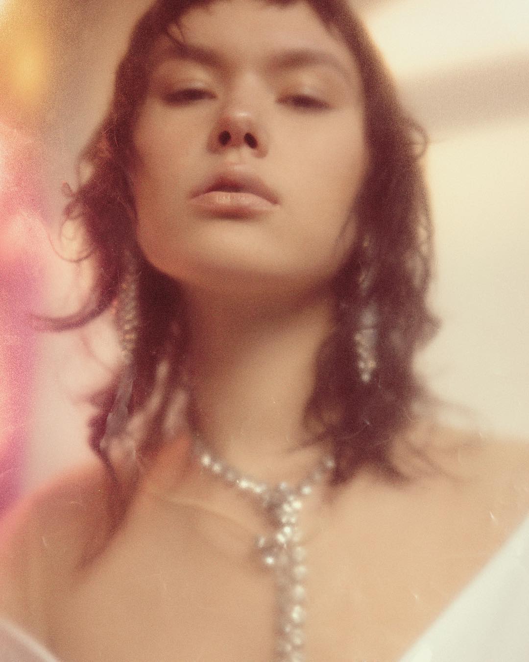 Close-up studio shot of an adult woman with dark hair wearing a crystal necklace and earrings with a neutral facial expression.