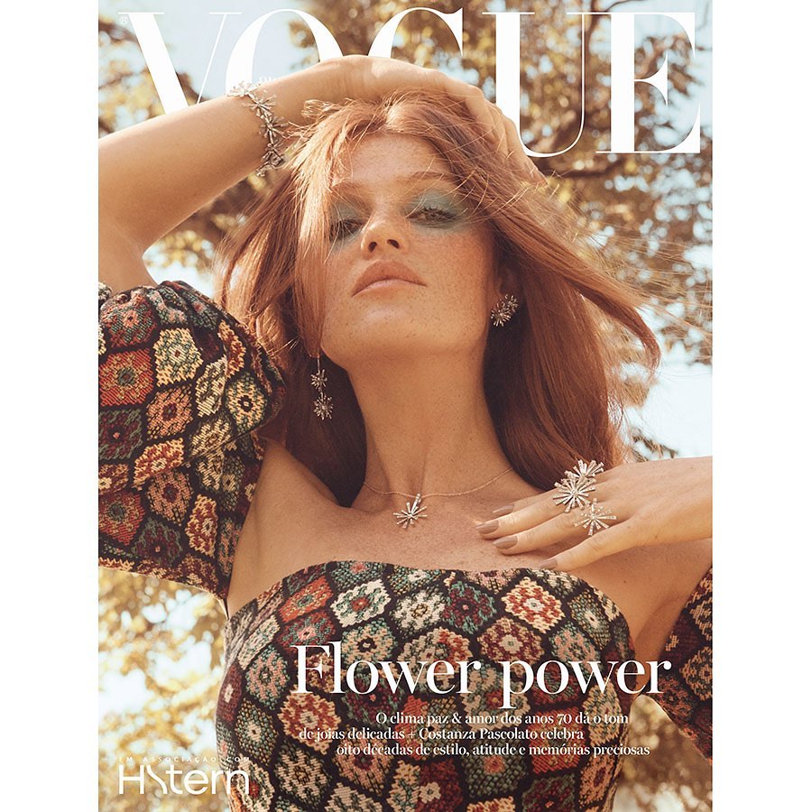 Vogue magazine cover featuring a model with red hair wearing jewelry and patterned top, posing outdoors in soft, diffused lighting.