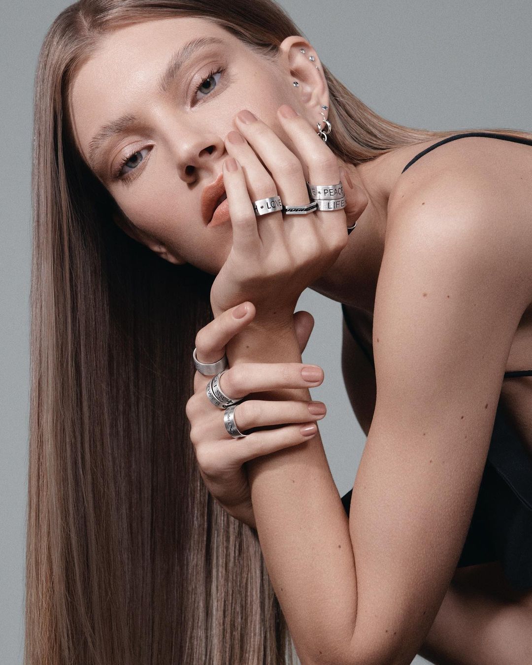 Close-up portrait of a woman with long straight brown hair wearing multiple silver rings photographed by Gil Inoue.