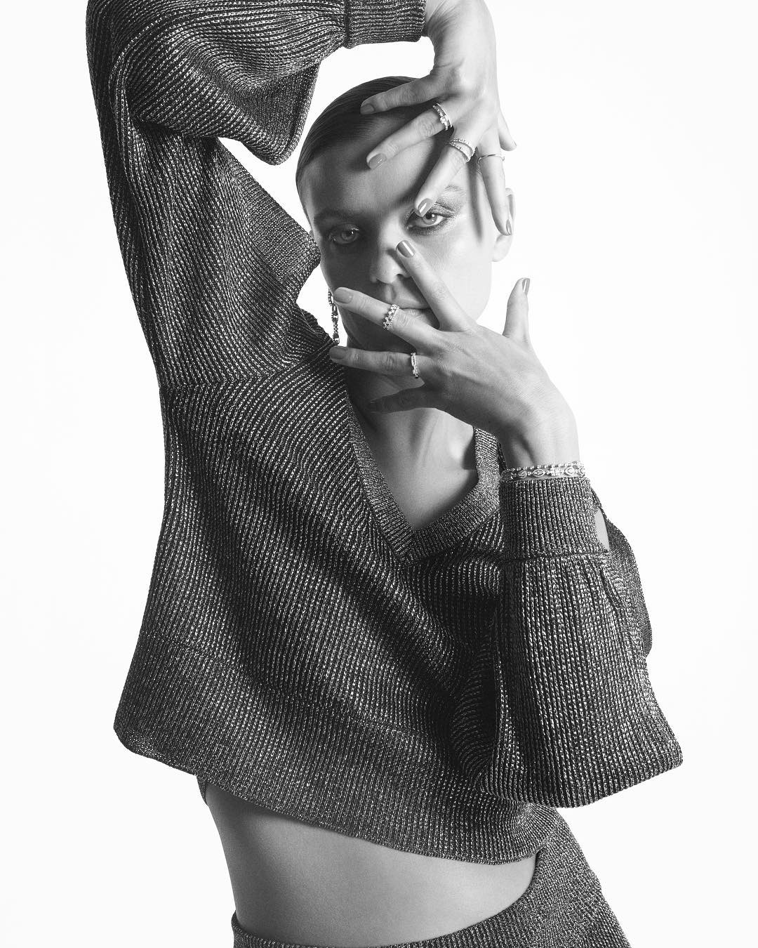 Monochrome portrait of a woman in a shimmering top, hands framing her face, in a bright studio setting, artistic fashion.