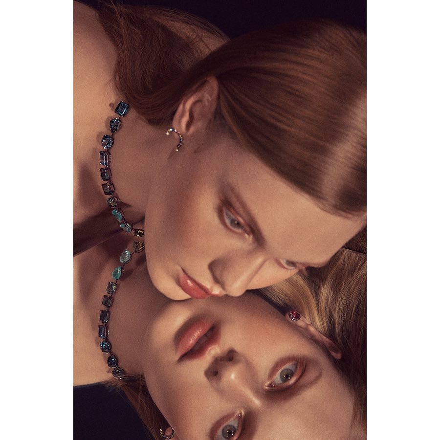Close-up of two fair-skinned women wearing jewelry, one with auburn hair, reflected against a dark backdrop, in a beauty or fashion context.