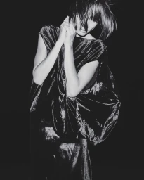 Black and white portrait of a woman wearing a dark velvet top with hands clasped near her face by photographer Gil Inoue.
