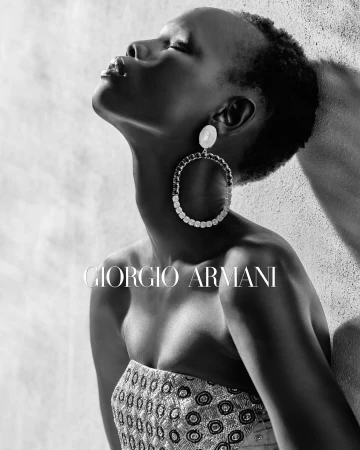 Black and white portrait of a woman wearing large jeweled hoop earrings and a patterned strapless top against a textured wall.