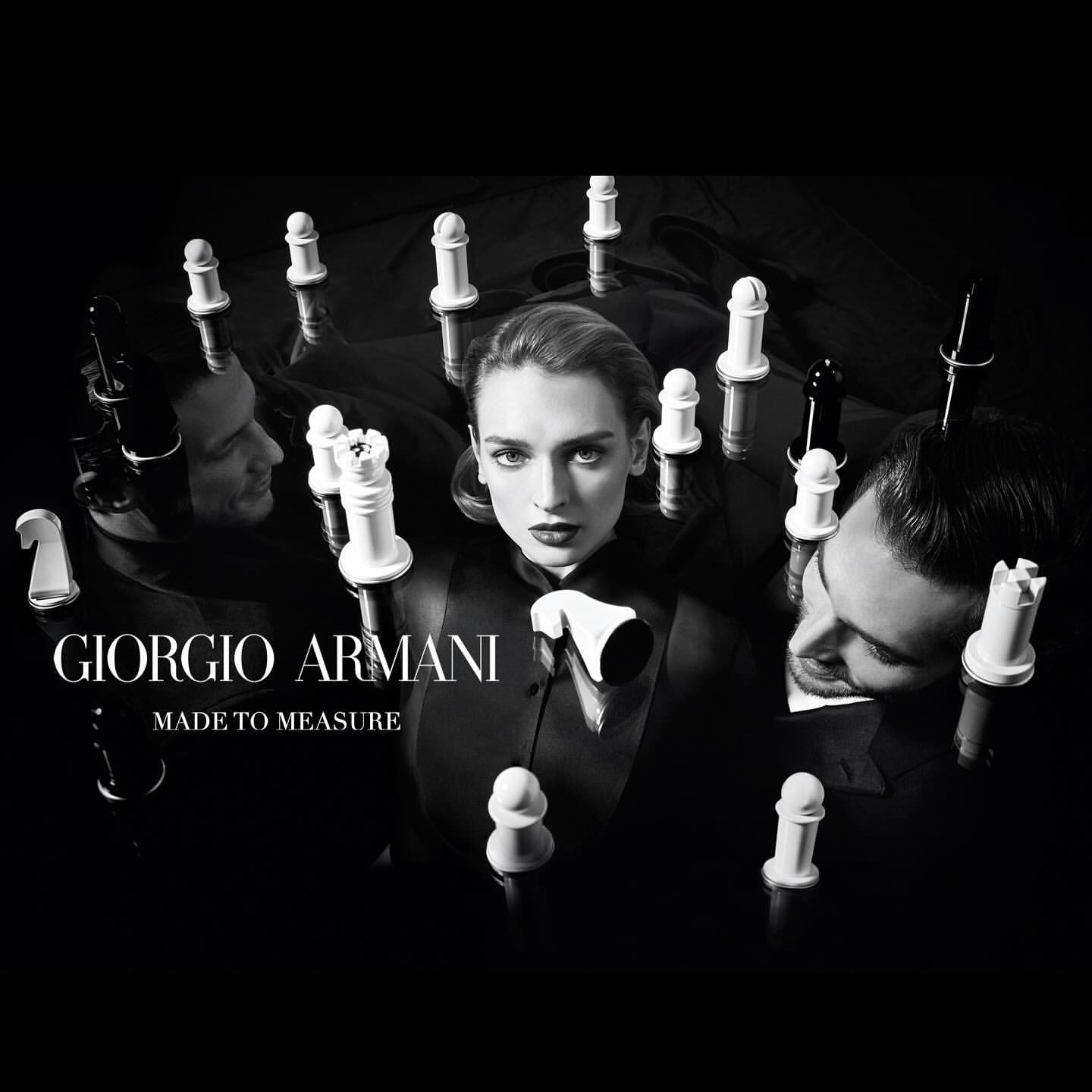 Black and white studio shot with a female model and two male models surrounded by chess pieces, promoting Giorgio Armani's Made to Measure.