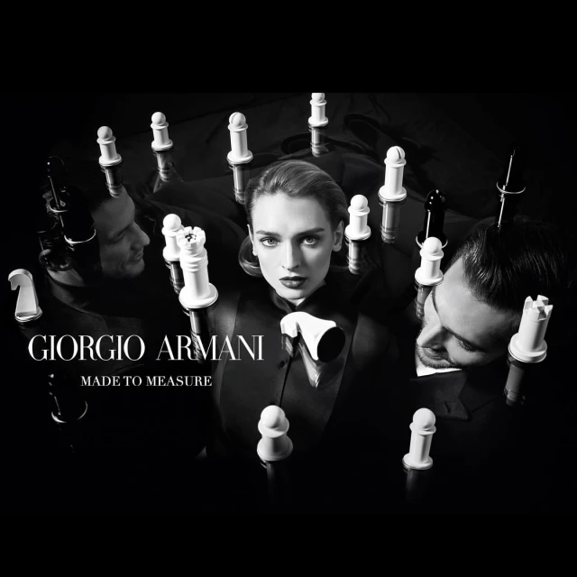 Black and white studio shot with a female model and two male models surrounded by chess pieces, promoting Giorgio Armani's Made to Measure.