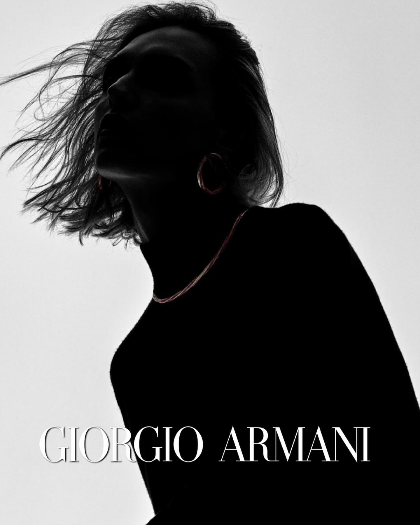 Silhouette of a person with flowing hair wearing hoop earrings and a fine chain necklace against a bright backdrop