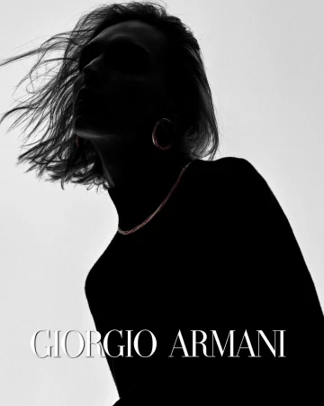 Silhouette of a person with flowing hair wearing hoop earrings and a fine chain necklace against a bright backdrop
