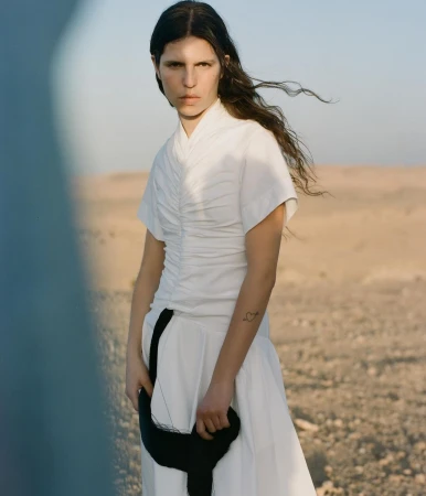 Model in white ruched dress with black strap standing outdoors in a desert landscape photographed by Giuseppe Triscari