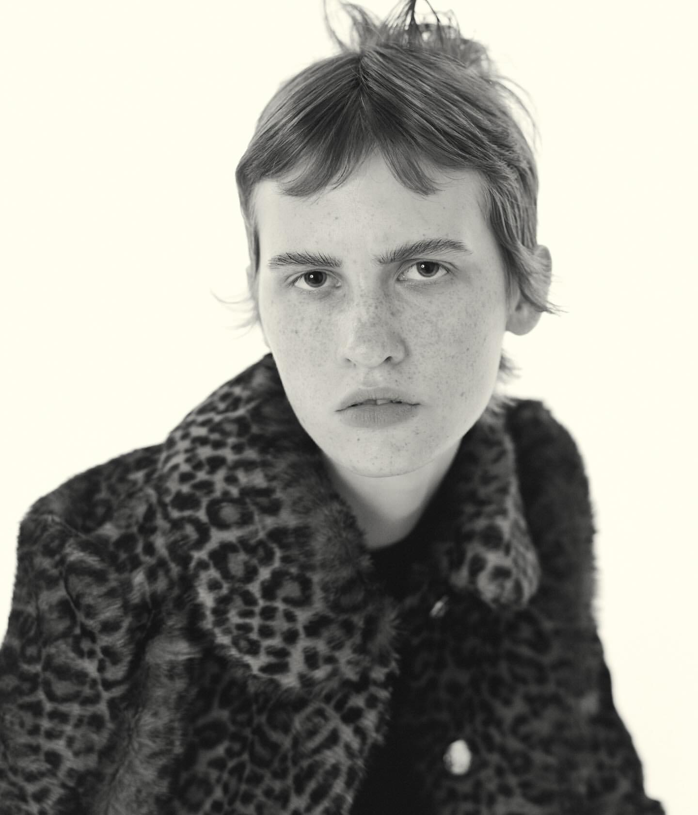 Portrait of a young adult woman with short hair wearing an animal print coat against a neutral backdrop in black and white.