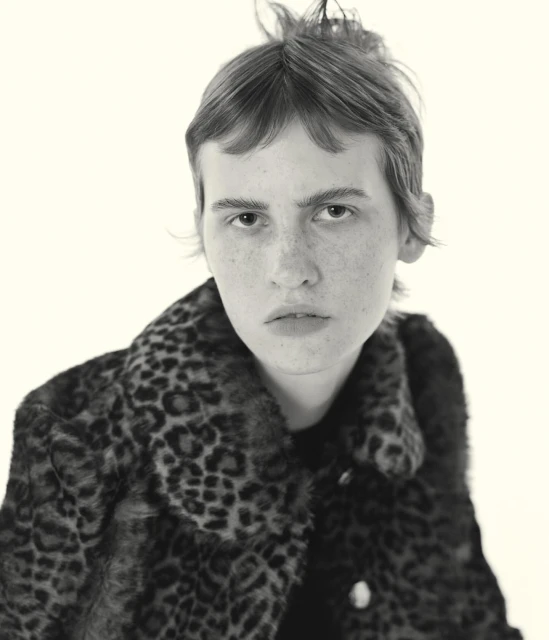 Portrait of a young adult woman with short hair wearing an animal print coat against a neutral backdrop in black and white.
