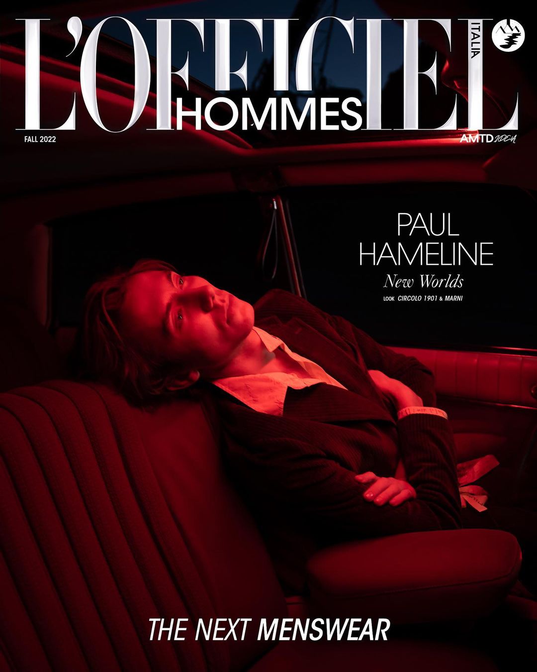 L'Officiel Hommes Italia magazine cover featuring a fair-skinned adult male in a suit, reclining in a car with red interior lighting.