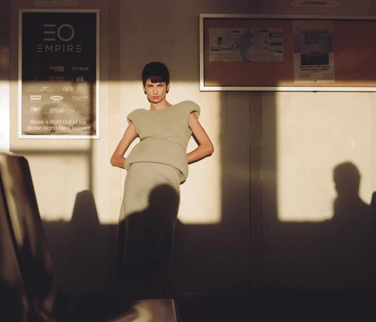 Fashion shot of a slender female model in a stylish, light-green outfit posing inside a building with sunlight and shadows.