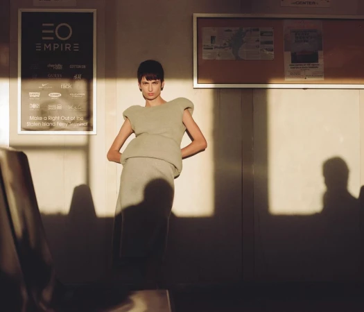 Fashion shot of a slender female model in a stylish, light-green outfit posing inside a building with sunlight and shadows.