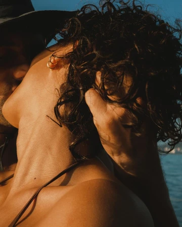 Close-up portrait of two people with sun-kissed skin embracing outdoors near water by Gleeson Paulino
