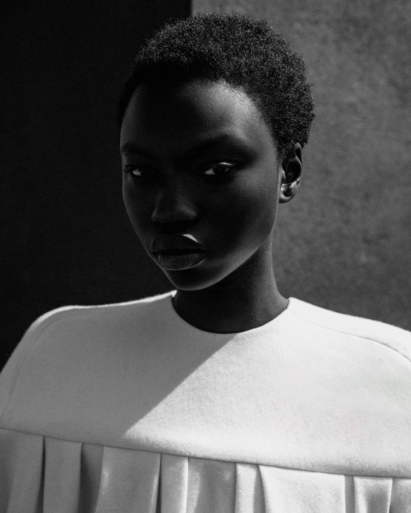 Striking portrait of a Black woman with short hair, wearing a white top, against a monochrome background, showcasing beauty and fashion.
