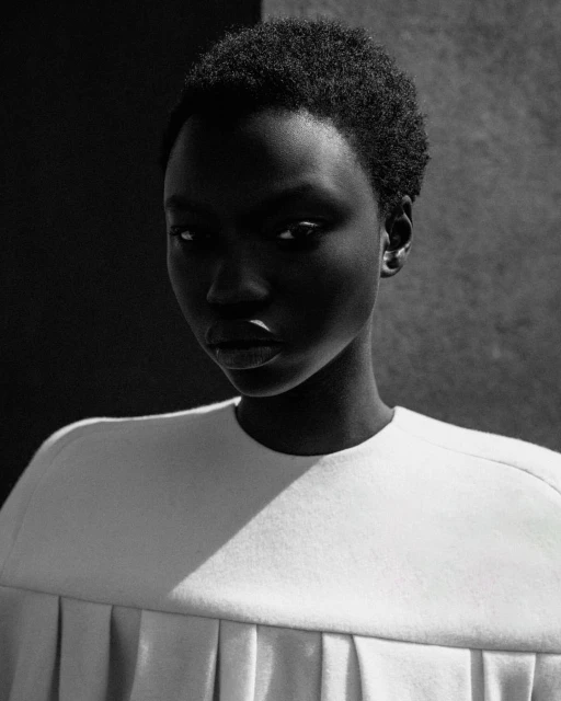 Striking portrait of a Black woman with short hair, wearing a white top, against a monochrome background, showcasing beauty and fashion.