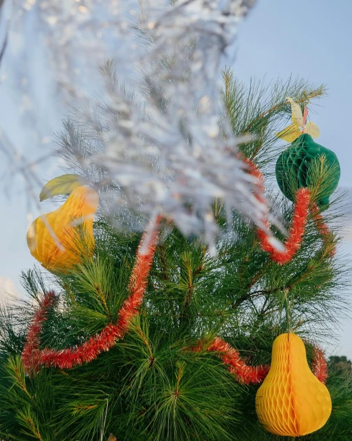 Christmas tree decorated with honeycomb ball ornaments and red garland. Festive holiday decorations on a green pine tree, soft blue background.