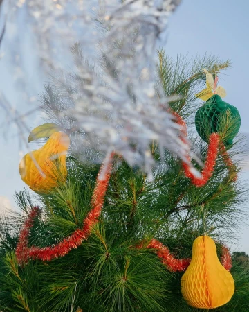 Christmas tree decorated with honeycomb ball ornaments and red garland. Festive holiday decorations on a green pine tree, soft blue background.