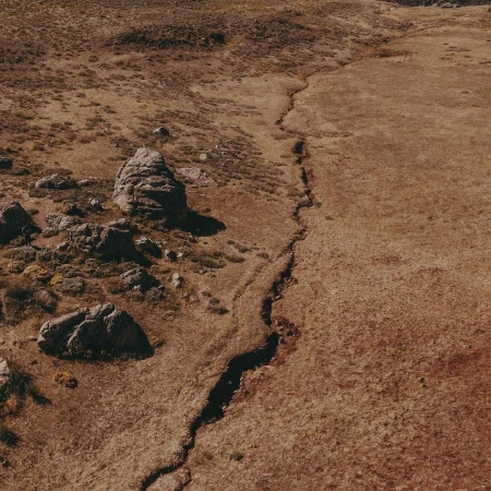 Aerial view of a dry, grassy landscape with rock formations and a deep crack running through the terrain, creating a textured, earthy scene.