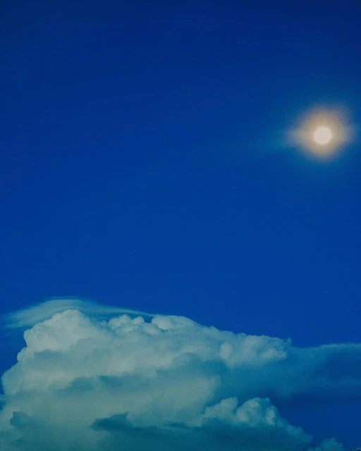 View of bright sun over white puffy clouds against a vivid blue sky. Weather concept, peaceful scene, and simple background.