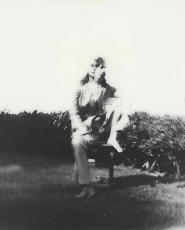 Portrait of a seated person outdoors captured in a grainy black and white aesthetic with multiple exposures.