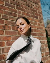 Woman in white shirt and black tie posing against red brick wall in New York portrait