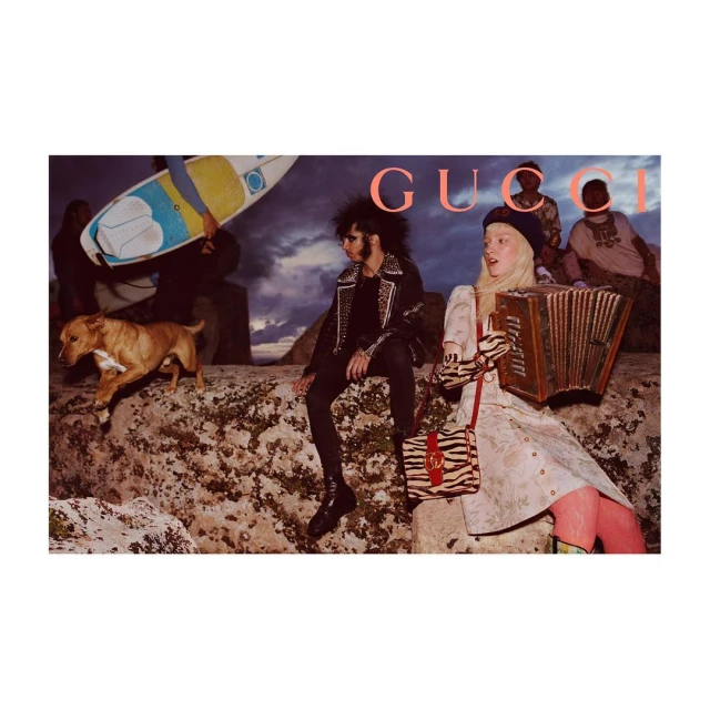 Fashion campaign featuring models in eclectic clothing with a surfboard and dog on a rocky landscape, overlaid with the brand name Gucci.