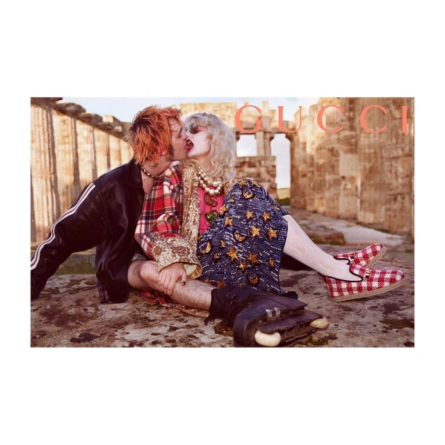 Fashion editorial image of a couple kissing while sitting on a stone surface outdoors at an ancient ruin, with designer clothes and accessories.