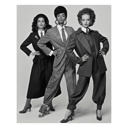 Three women in suits stand in a studio with neutral lighting. The black and white photo features models in vintage-inspired power suits.
