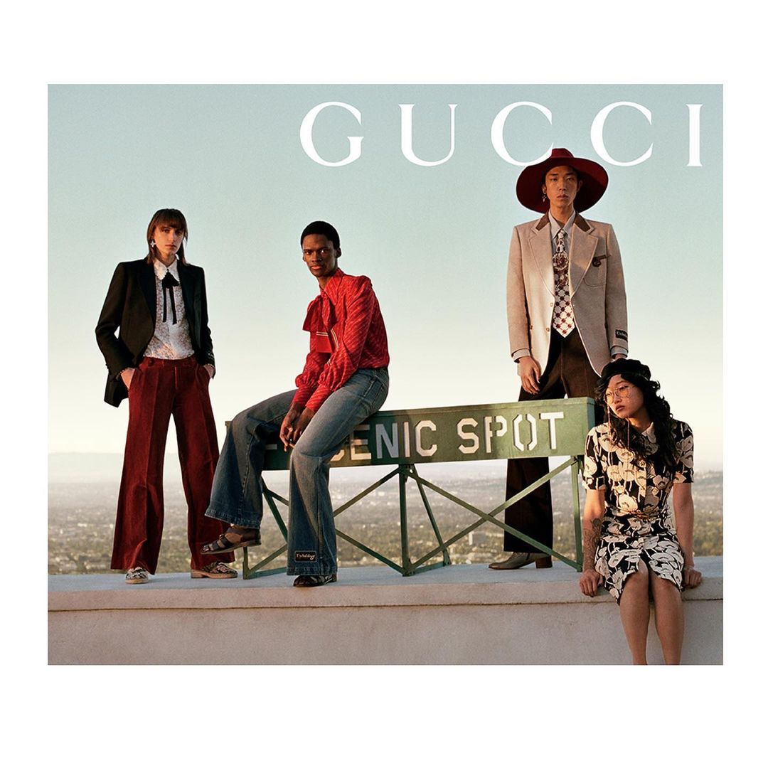 Four people in Gucci apparel pose on a scenic overlook against a background of city buildings and a light blue sky.