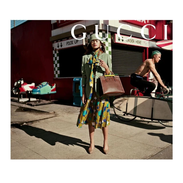 A woman in a floral dress and blazer poses with a purse, while a man rides a bike with a surfboard in a fashion editorial shot.