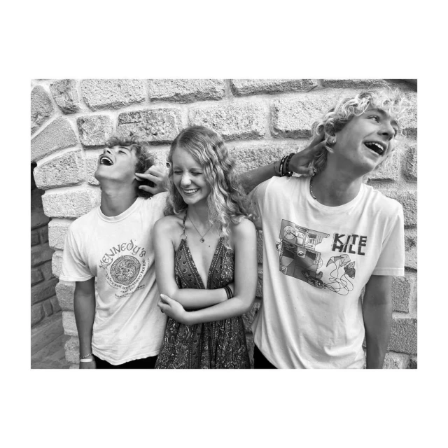 Black and white portrait of three young adults laughing together in front of a stone wall, conveying happiness and friendship.