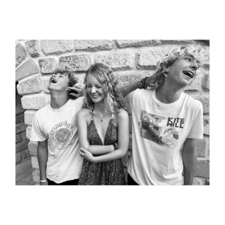 Black and white portrait of three young adults laughing together in front of a stone wall, conveying happiness and friendship.