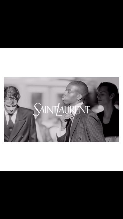 Black and white fashion-editorial shot featuring three people and the Saint Laurent logo in the foreground. Classic formalwear.