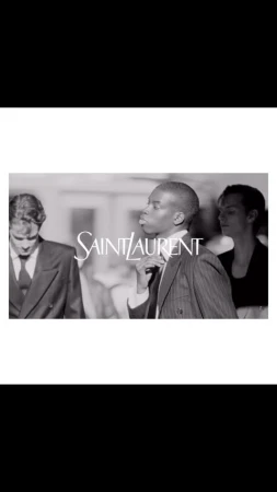 Black and white fashion-editorial shot featuring three people and the Saint Laurent logo in the foreground. Classic formalwear.