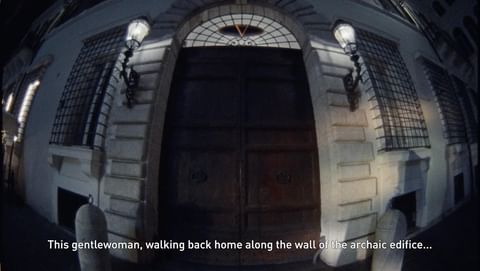 Exterior shot of a building at night with a large wooden door, decorative sconces, and wrought iron window grates.