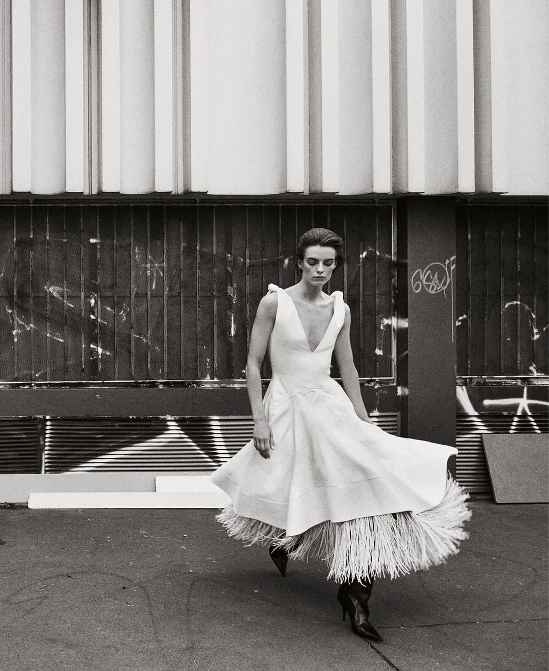 Model in white dress with fringed hem walking outdoors by Glen Luchford