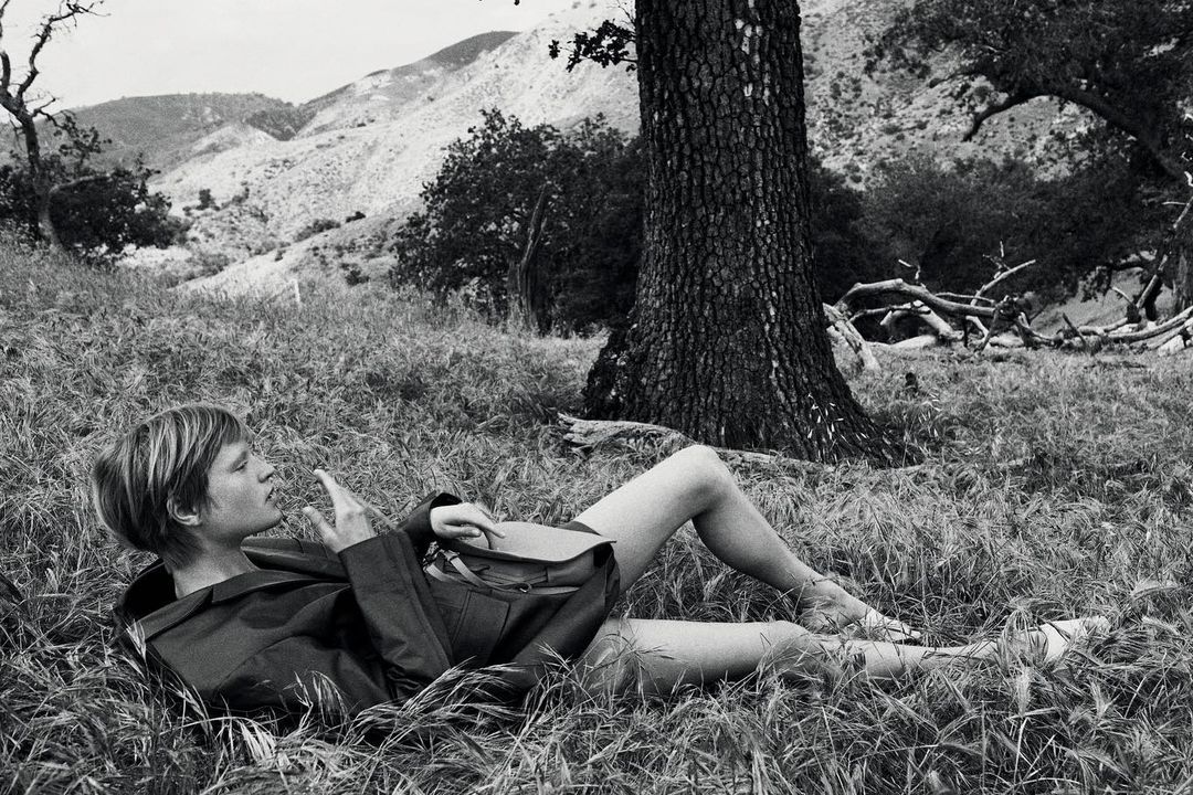 Monochrome image of a woman lying in tall grass beneath a large tree in a natural landscape shot by Glen Luchford