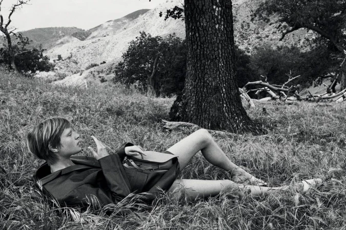 Monochrome image of a woman lying in tall grass beneath a large tree in a natural landscape shot by Glen Luchford
