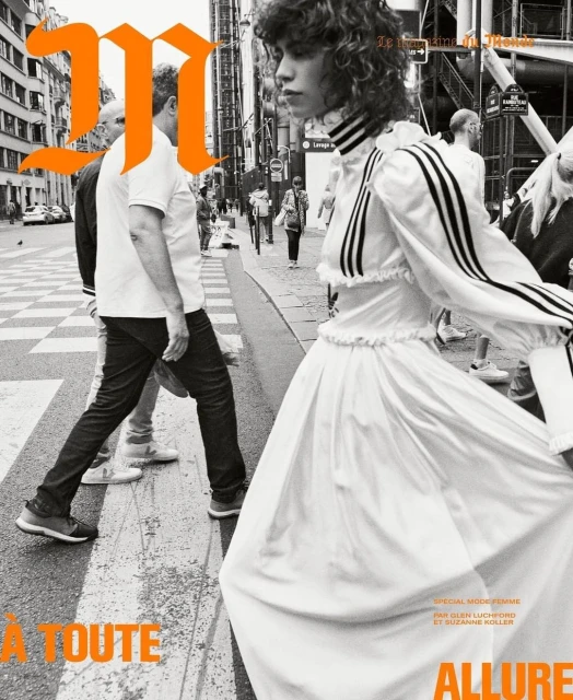 Fashion editorial featuring a model in a white dress on a crosswalk in Paris, with onlookers and large magazine branding.