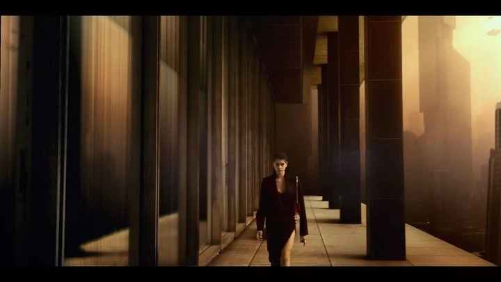Woman in dark clothing walking along a colonnade walkway with tall columns and a hazy city skyline background.