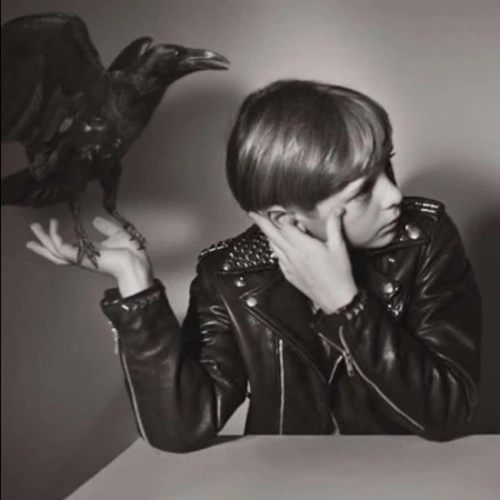 Monochrome shot of person in studded leather jacket with a raven perched on their hand against a neutral background.
