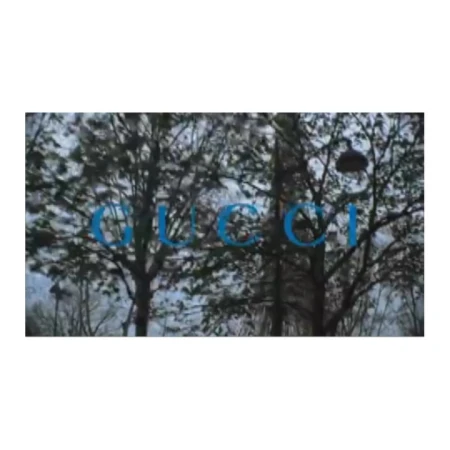 A still from a video by Glen Luchford showing bare trees under an overcast sky with blue Gucci brand text overlaid.