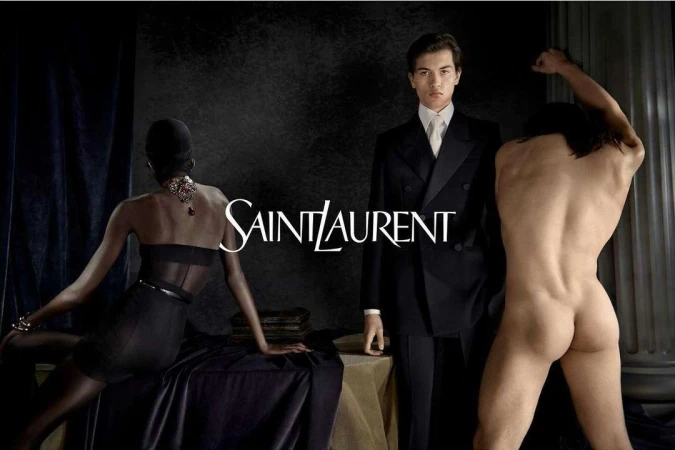 Black and white fashion shot featuring two models flanking a model in a suit against a dark background with the Saint Laurent logo.