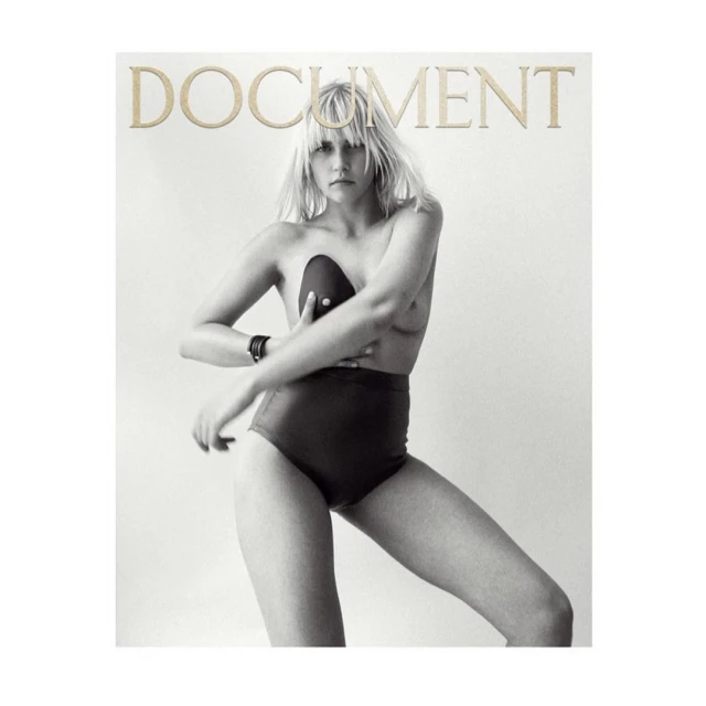 Black and white studio shot of a Caucasian woman posing in high-waisted bottoms, with a black bra, and the word 'DOCUMENT' at the top.