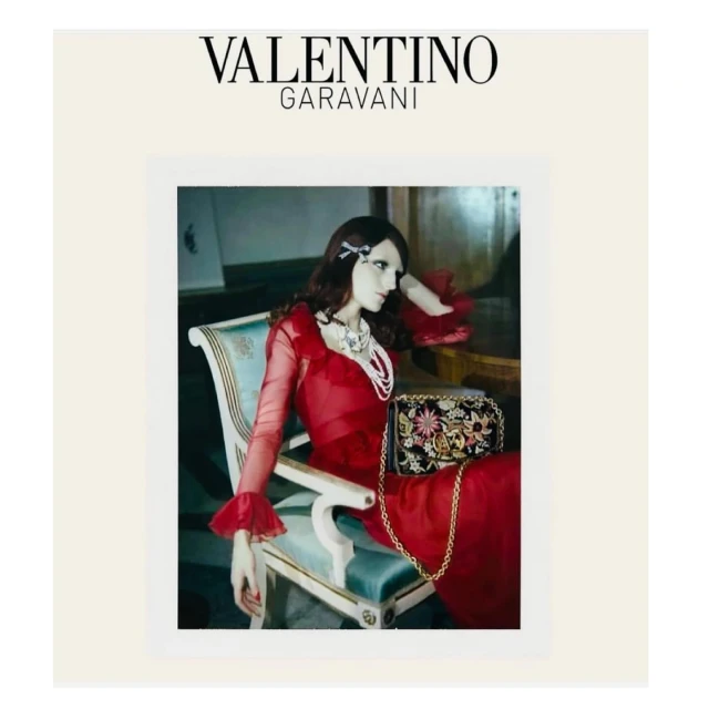Elegant mannequin seated in chair, adorned in red gown and pearl jewelry, with a floral purse in a vintage-inspired fashion photo.