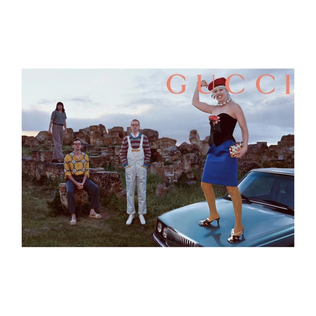 Fashion editorial featuring a group of five adults in an outdoor setting near a car and stone ruins under a cloudy sky at dusk.