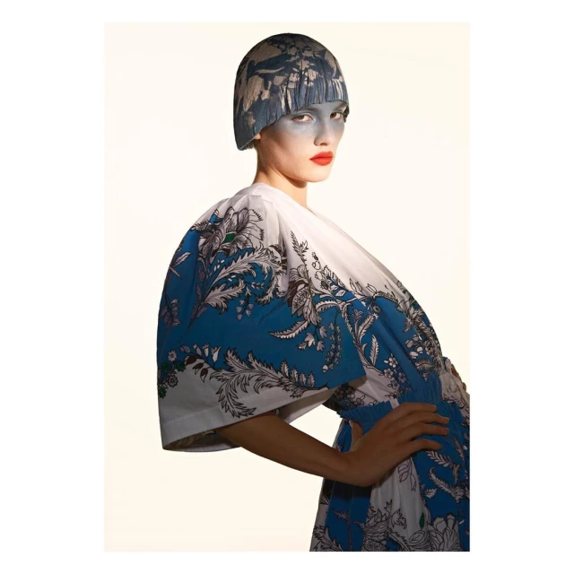 Fashion portrait of a model wearing a patterned dress and head covering against an off-white background, showcasing editorial design.
