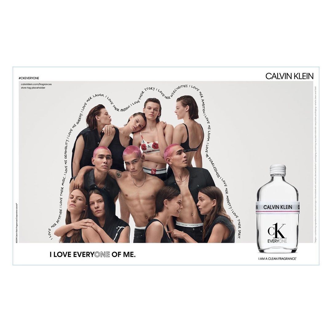 Calvin Klein ad features a group of young adults posing together with a Calvin Klein fragrance bottle. Light background and text accents.